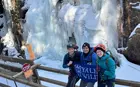 Three people posing next to a frozen waterfall