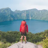 Man in red jacket at the top of a mountain overlooking lake