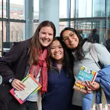 Three students holding books and smiling