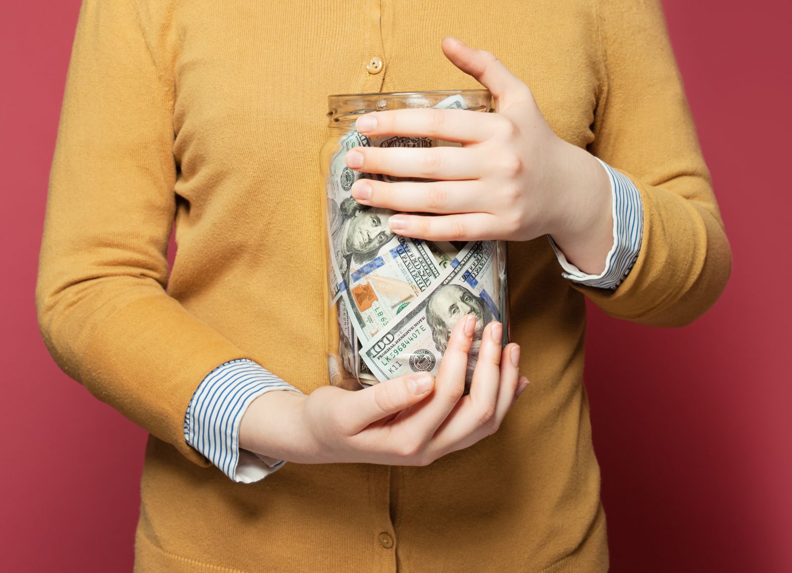 person in yellow sweater holding a glass jar of cash