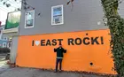 Joao Rocha in front of sign painted on side of a building that reads "I Love East Rock"