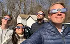 A group of students outside, wearing eclipse glasses and looking at the sky