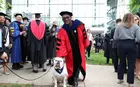 A person in a red academic robe posing with a bulldog in front of Evans Hall
