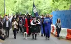 A procession of students led by a bagpiper, a bulldog, and a person with a sign reading "School of Management"