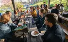 A group of people eating pizza at an outdoor picnic table