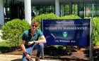 A student kneeling in front of a sign that says "Yale University School of Management"