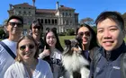 Several people posing in front of a large house with a dog