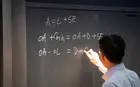 A photograph of a person writing on a blackboard