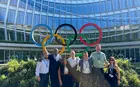 Several people posing outside an office building with the Olympics logo