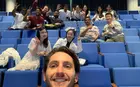 A person taking a selfie in an auditorium with several people posing in the background