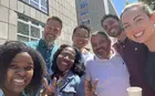 Several people posing for a group selfie outside an office building