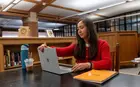 A person sitting at a table in a library working on a laptop