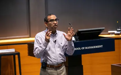 A professor lecturing with raised hands in front of a chalkboard