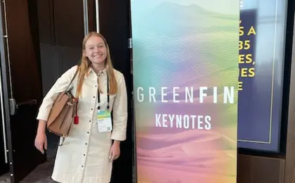 A student wearing a white dress standing next to a sign that says "Greenfin Keynotes"