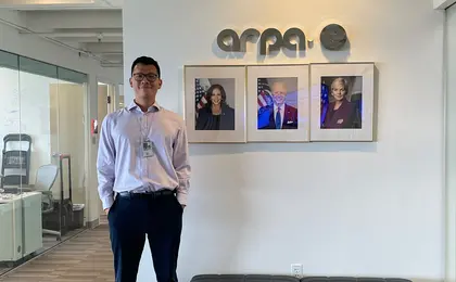 A student standing in an office with the acronym "ARPA-E" displayed on the wall