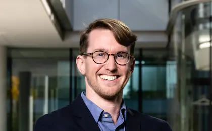 A person wearing a suit smiling with folded arms