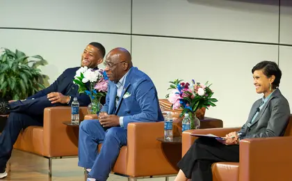 Three speakers sitting in chairs on a stage