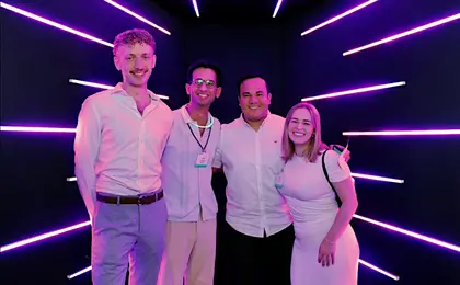 Four people standing against a dark background surrounded by purple neon lights