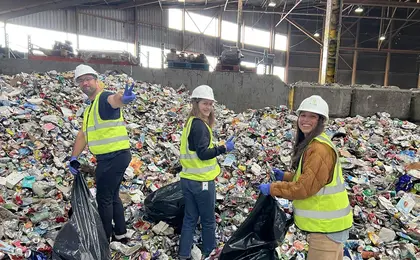 Three people wearing reflective vests and hard hats cleaning up a large pile of trash