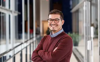 A smiling person wearing a red sweater posing with their arms folded