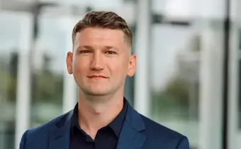 A headshot of a person wearing a suit against a glass wall