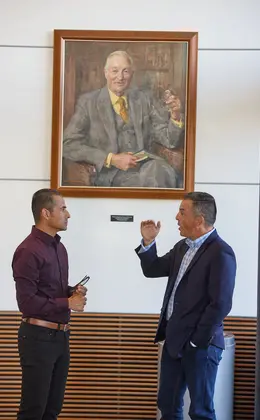 Two Fellows standing and talking in front of large portrait