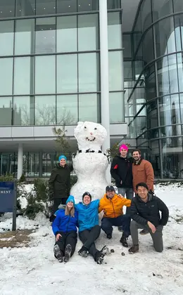 A group of people posing with a snowman in front of Evans Hall