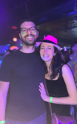 Two people wearing glow-in-the-dark face paint posing in a dark room