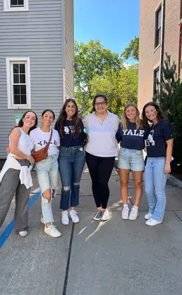 Six people standing on a sidewalk with residential buildings in the background