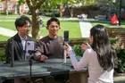 Three students sitting at a picnic table filming a video with their phones