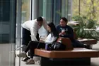 Three people seated on a square bench looking at a laptop