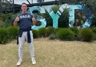 A person wearing a Yale t-shirt and giving a thumbs-up sign stands in front of a large sign that says “SYD”