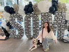 A person posing with a dog in front of a large decorative sign that says “SOM”