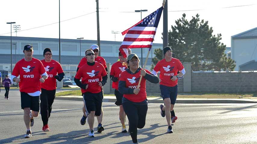 A group of people in identical dress running with an American flag