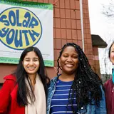 group of three people outside a building with a sign that reads “Solar Youth”