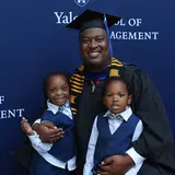Master's graduate with twin children, in front of Yale SOM step and repeat