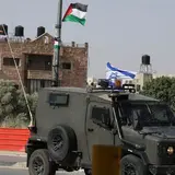 Military vehicle flying Israel flag past buildings