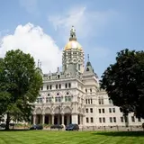 Outside view of the Capitol building in Hartford CT with green trees and grass in the foreground.