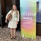 A student wearing a white dress standing next to a sign that says "Greenfin Keynotes"