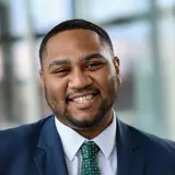 A headshot of a smiling person wearing a suit jacket and tie