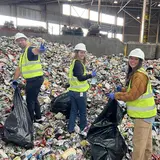 Three people wearing reflective vests and hard hats cleaning up a large pile of trash