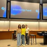 Three people standing at the front of an auditorium, under three screens that say “Internship Fund”