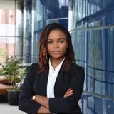 A person wearing a white suit and dark jacket standing with folded arms