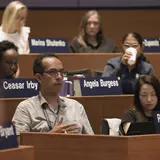 Several people seated at desks in an auditorium, with one person talking